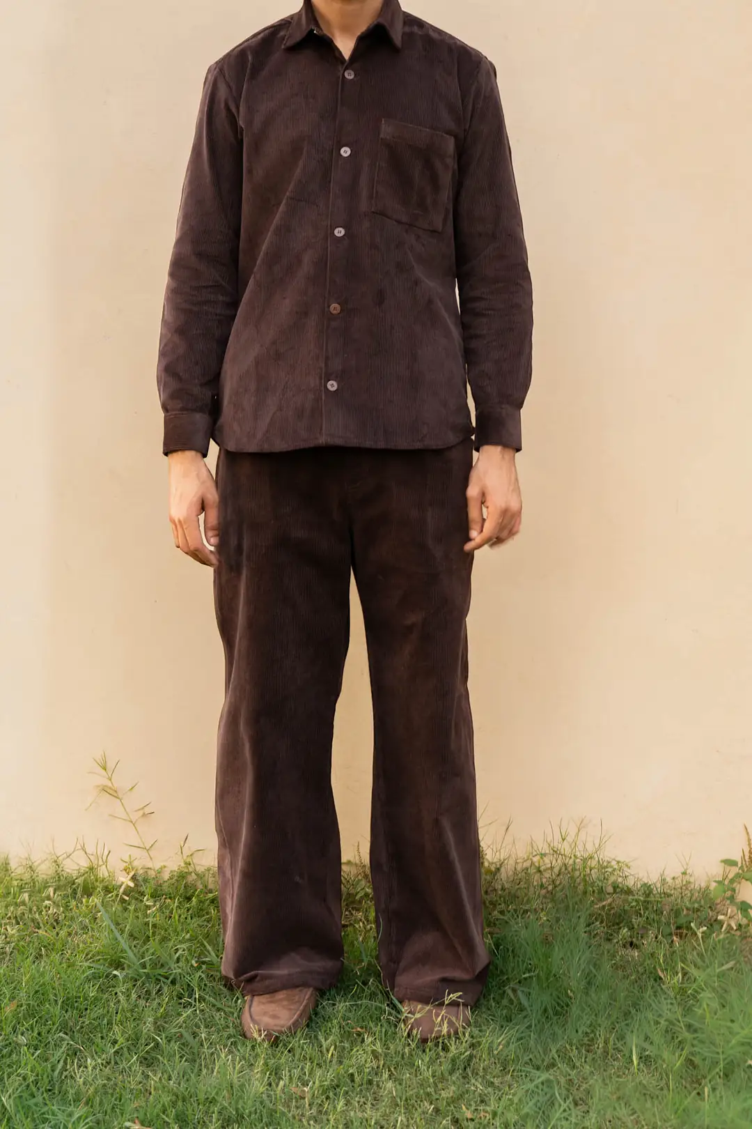 A man in a dark brown corduroy overshirt, matching wide-leg corduroy trousers and brown suede loafers